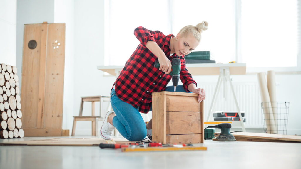 Indoor shot of young woman repairing furniture at home, sitting on the floor.